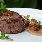 Beef tournedos/filet medallion with a mushroom and cream sauce and microgreens on a white plate
