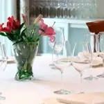 Set dining table with white linen, wine glasses and a vase of red and pink flowers in a bright dining room