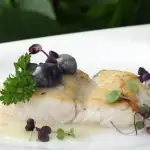Pan-seared white fish fillet with blueberries, sauce and microgreens on a white plate