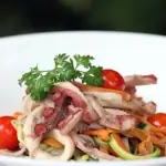 Squid salad with julienned vegetables, cherry tomatoes and parsley on a white plate