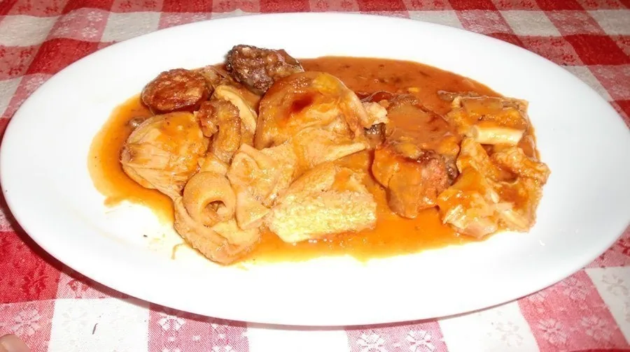 A white oval plate of pieces of meat in a tomato sauce on a checked cloth