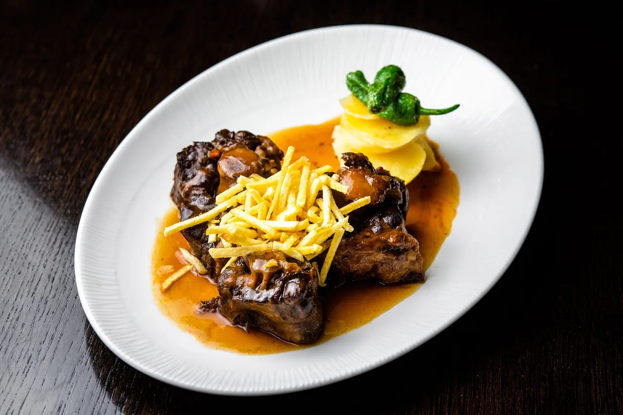 Braised oxtail topped with fine potato strips on a white plate