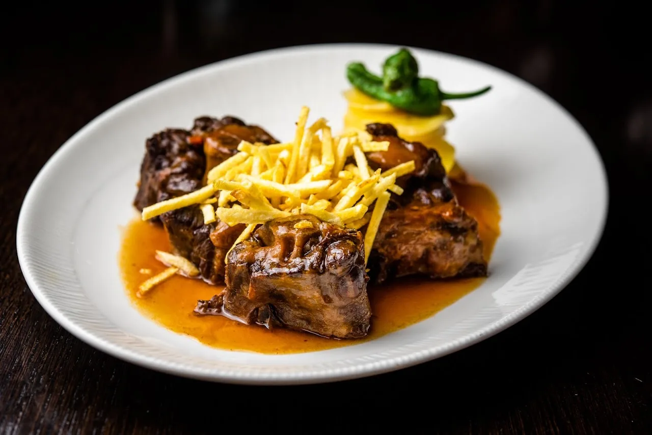 Braised meat pieces in a rich sauce topped with matchstick fries and a fried green pepper on a white plate
