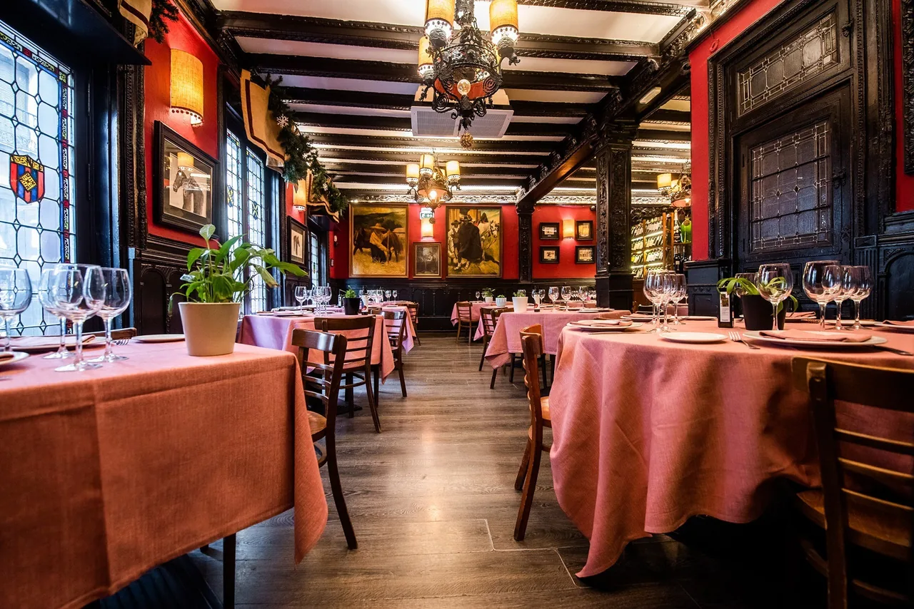 A dining room with red walls, dark wood beams and windows, and tables covered in pink cloths.