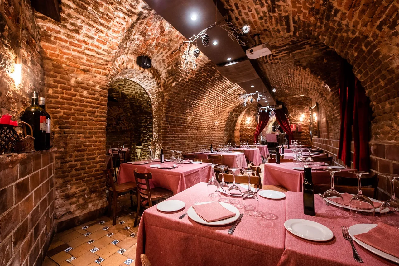 A brick-vaulted cellar dining room with tables set with pink tablecloths.