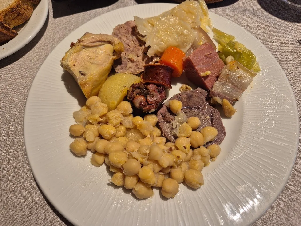 A white plate of stewed chickpeas with cabbage, potato and cuts of meat.