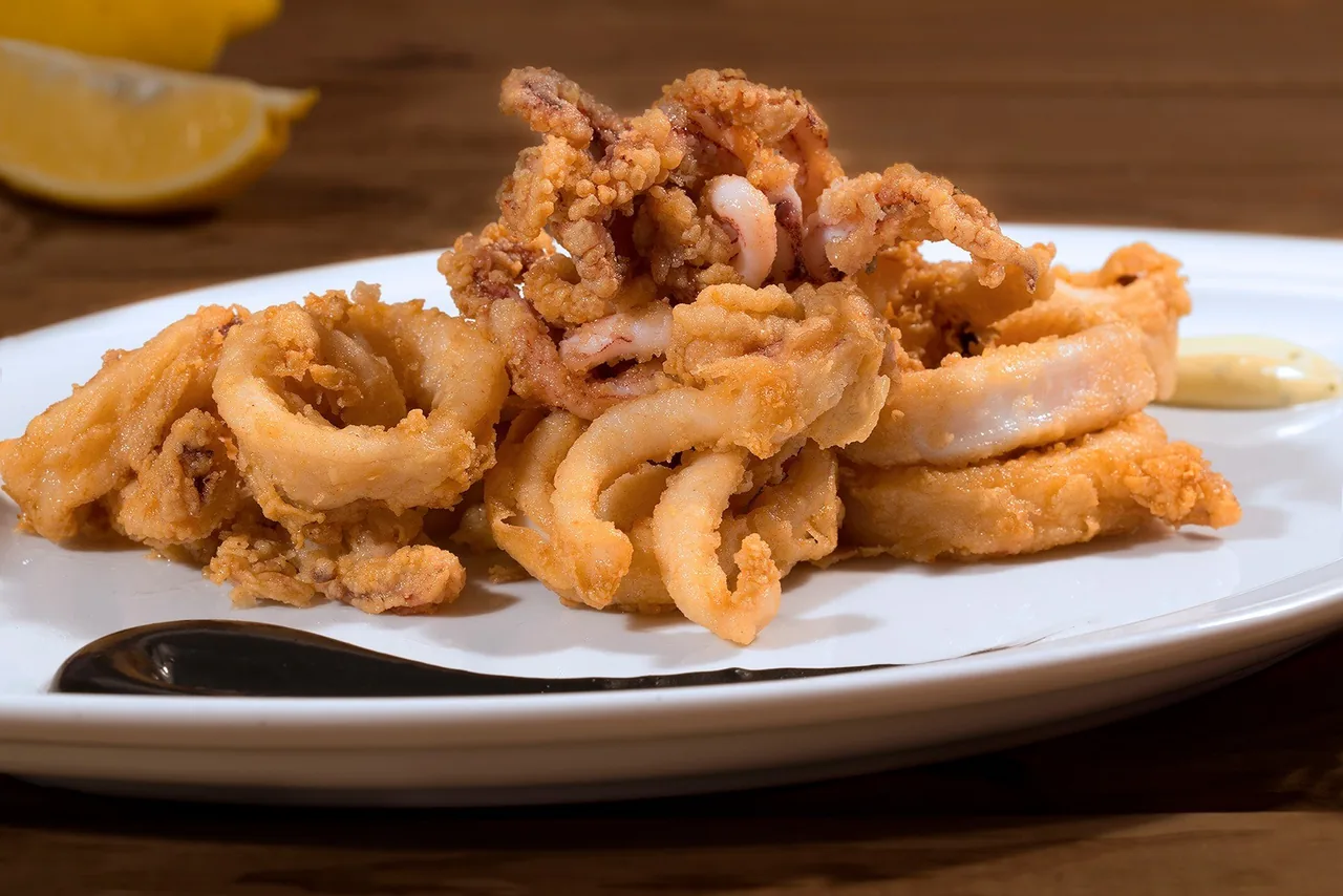 A white plate of fried squid rings with a lemon wedge