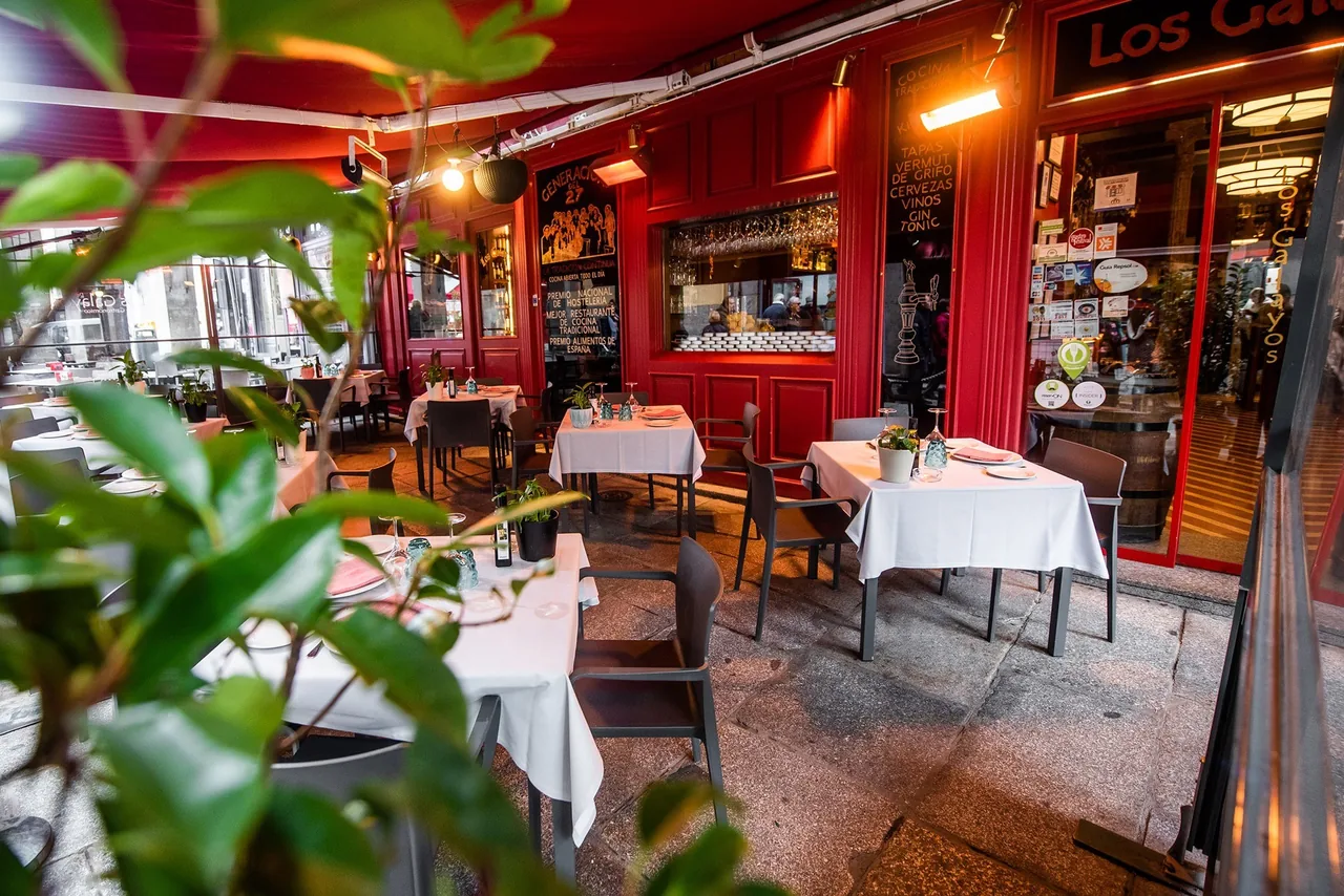 Outdoor terrace tables seen through green leaves beside a red restaurant frontage