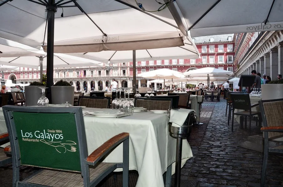 Terrace tables with white tablecloths under parasols on a cobbled square