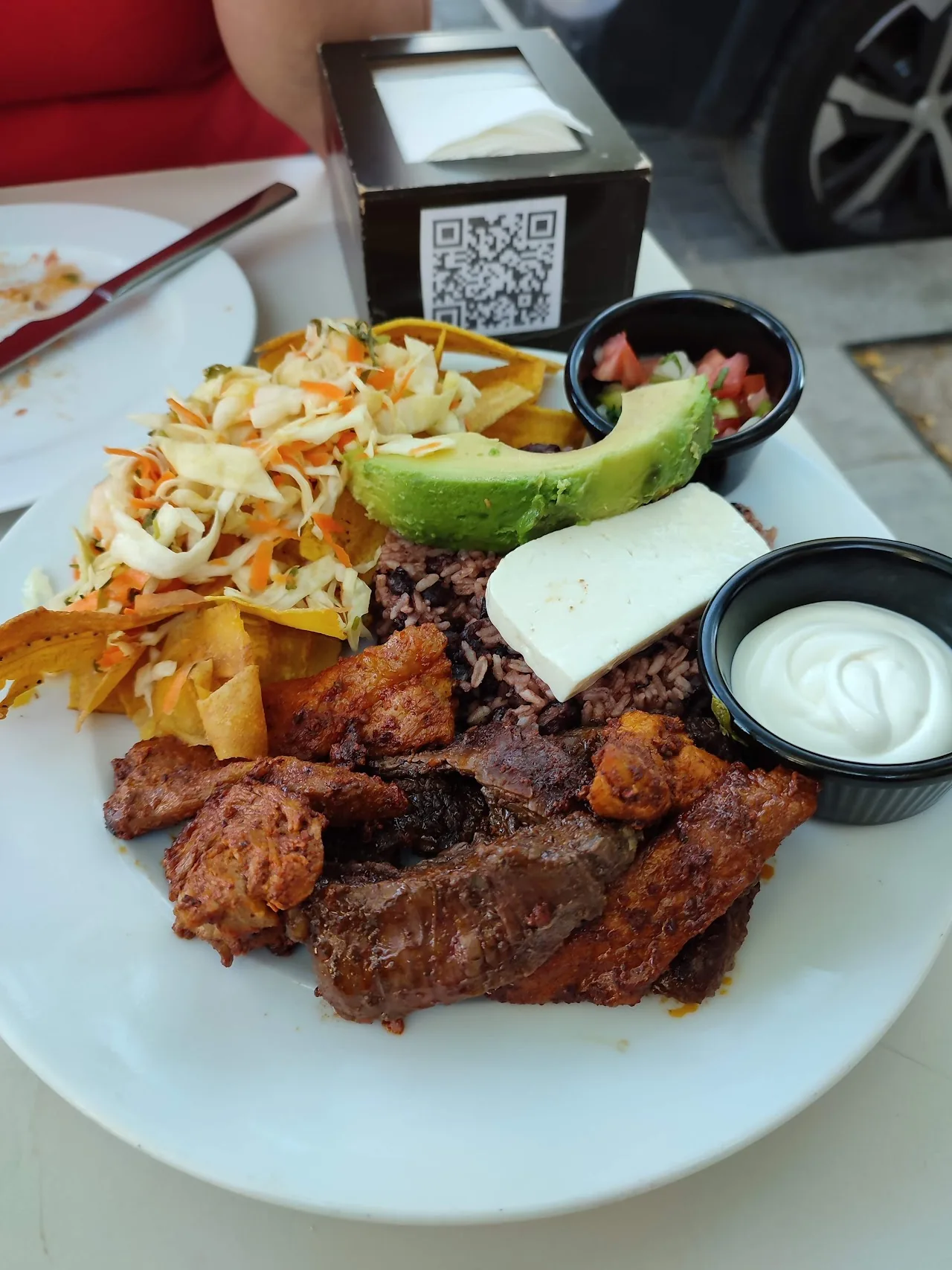 A mixed grill plate with meat, avocado, and sour cream