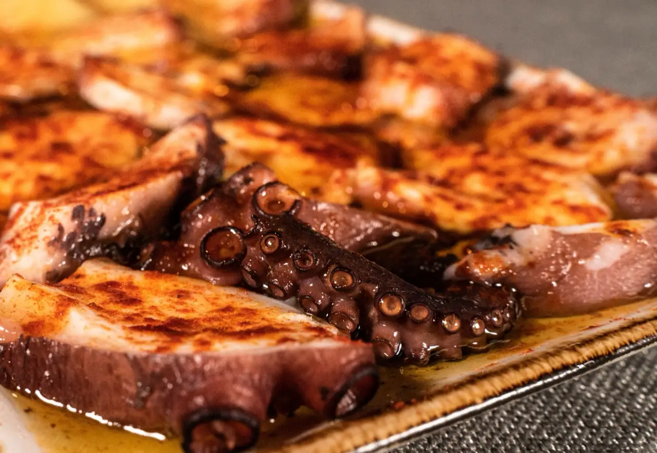 Pulpo a la gallega, slices of octopus dusted with paprika and drizzled with olive oil on a wooden plate
