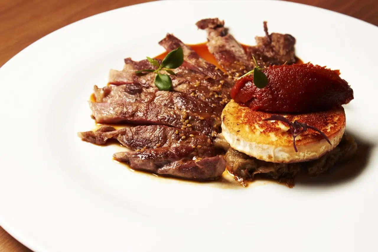 Sliced seared beef with sesame, a seared round of cheese and a quenelle of red purée on a white plate