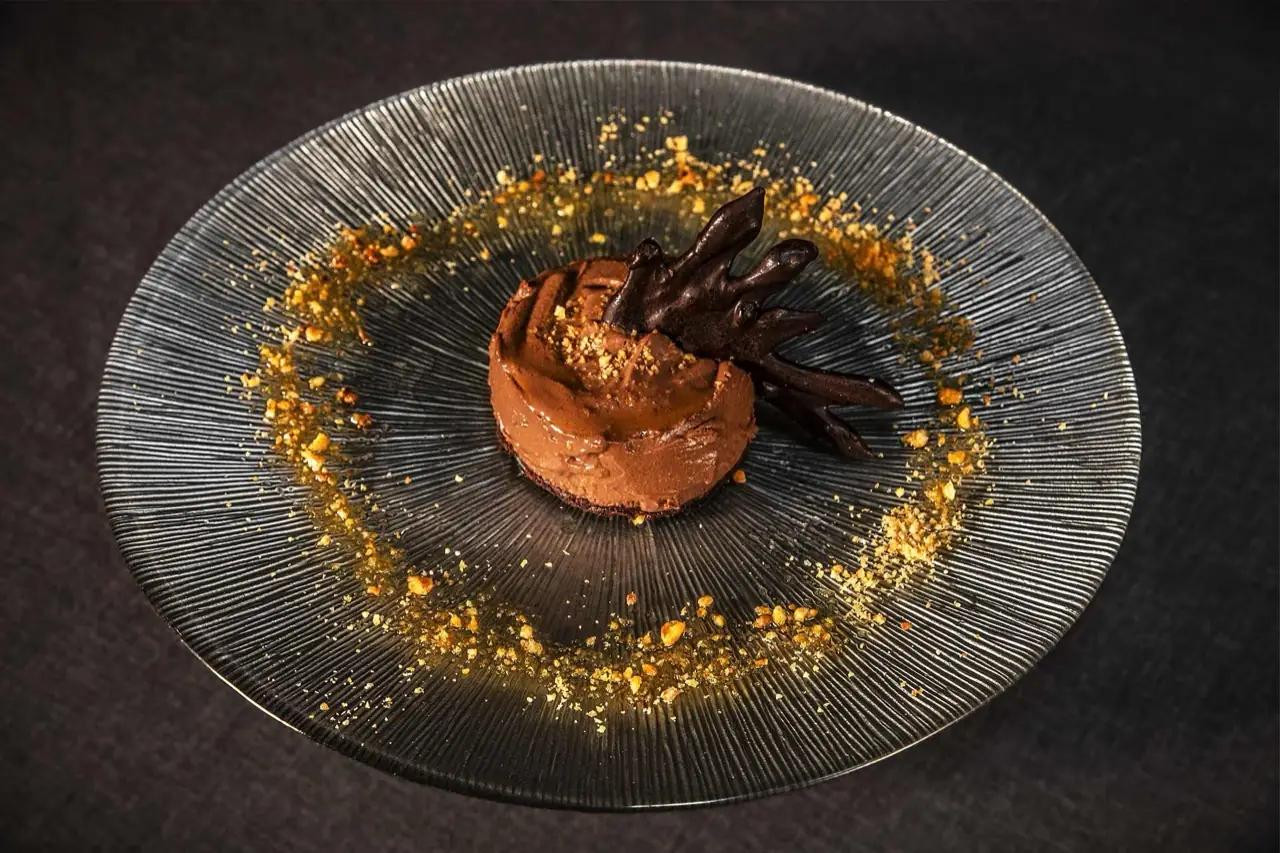 Chocolate mousse dessert with a chocolate garnish and a ring of golden crumble on a ridged glass plate