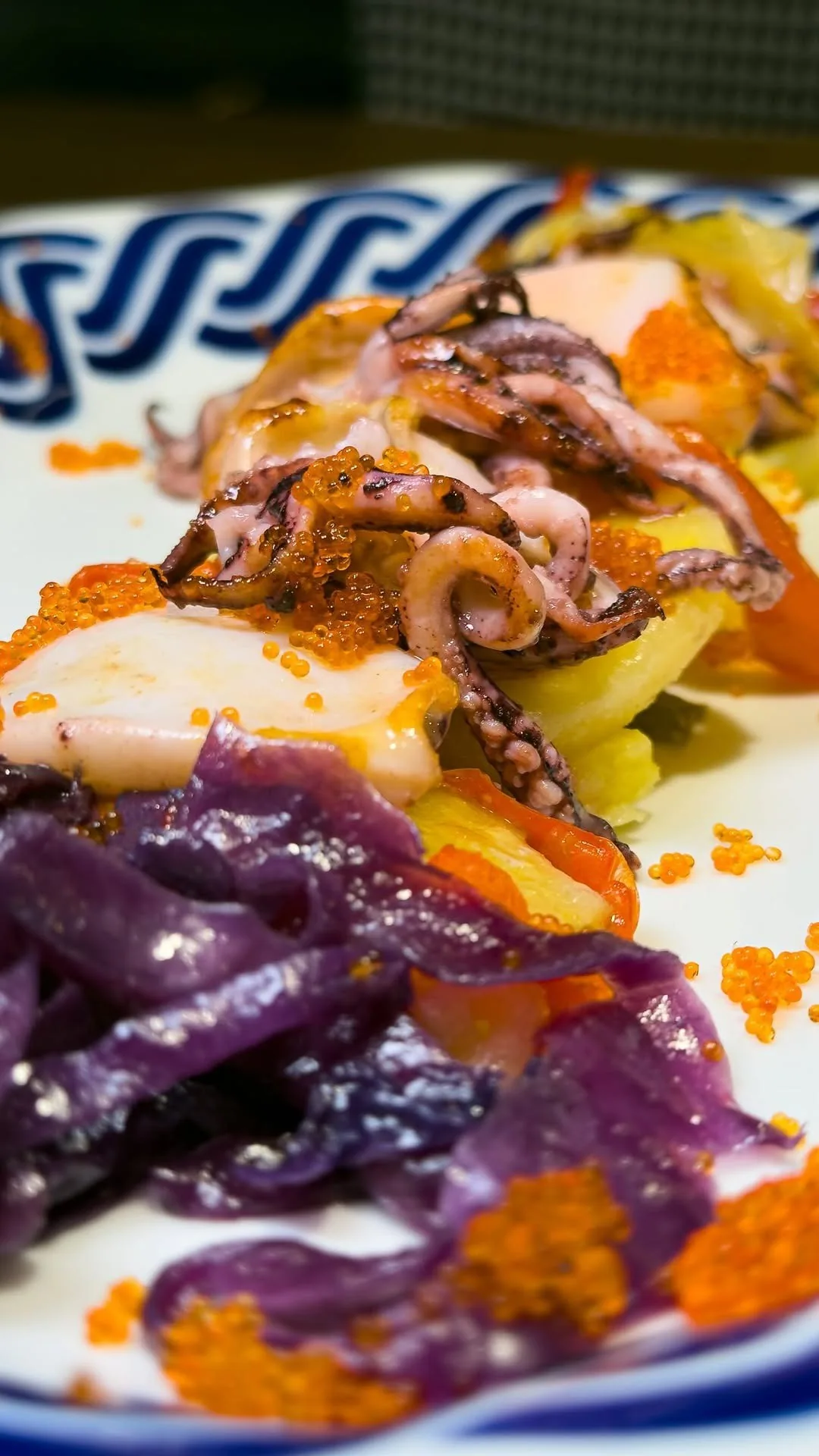 An octopus dish with colourful garnish on a patterned plate