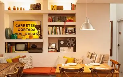 Interior with built-in bookshelves holding books, vintage TV and film reel, a yellow road-sign decoration, and a cushioned banquette beside a set wooden table