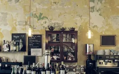 Bar area with distressed yellow patina walls, hanging Edison bulbs, shelved liquor bottles, an espresso machine and a small chalkboard
