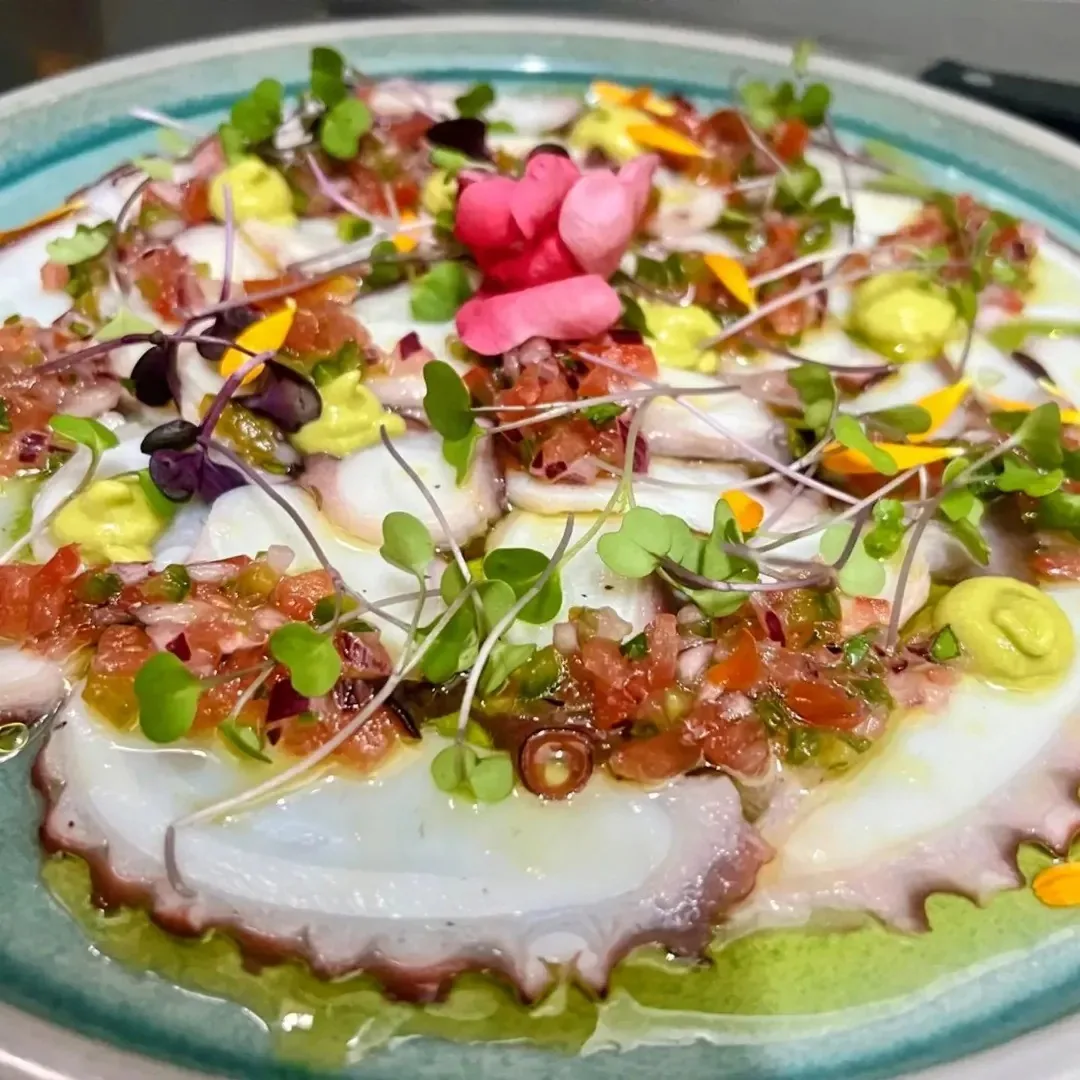 A plate of sliced seafood topped with colourful edible flowers and microgreens