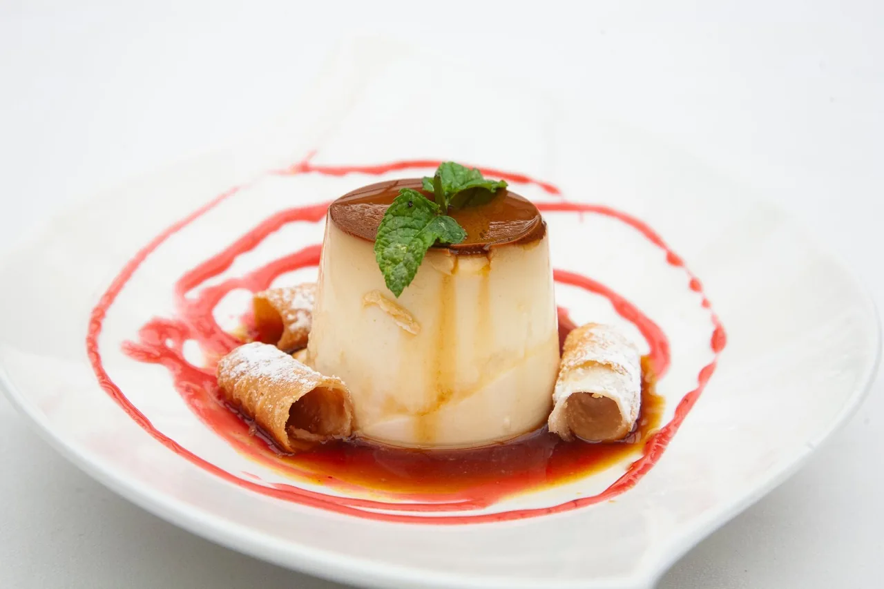 A pale cream dessert on a white plate with red sauce