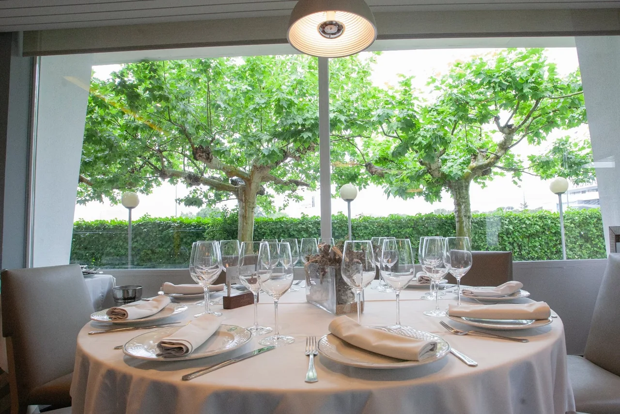 A round table set for a meal beside a large window with trees outside