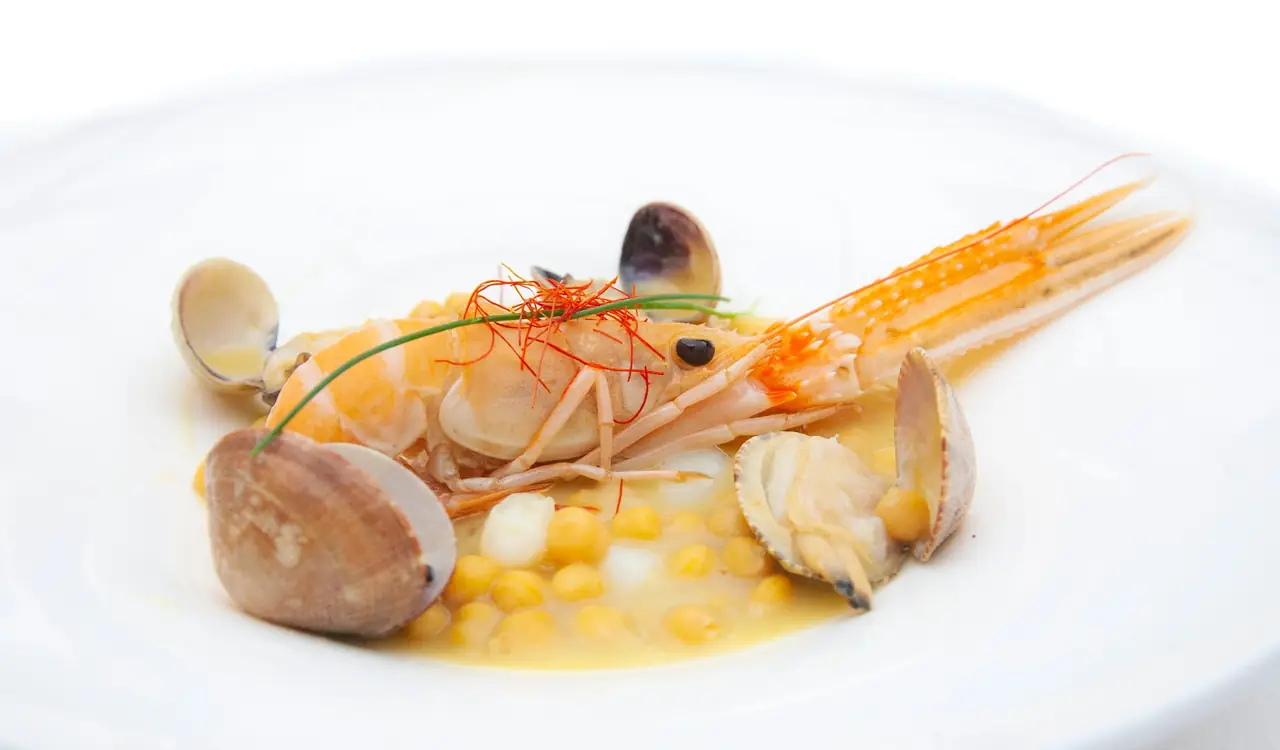 Close-up plated dish of a langoustine with clams and chickpeas in a light broth, garnished with saffron threads