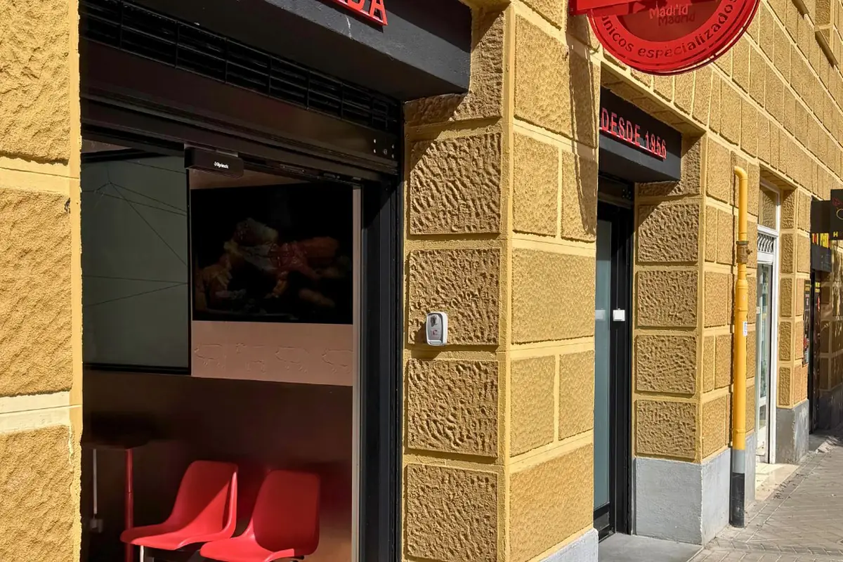 Ochre-stone facade of Los Torreznos with a window seating nook of red stools and a red circular 'Desde 1966' sign