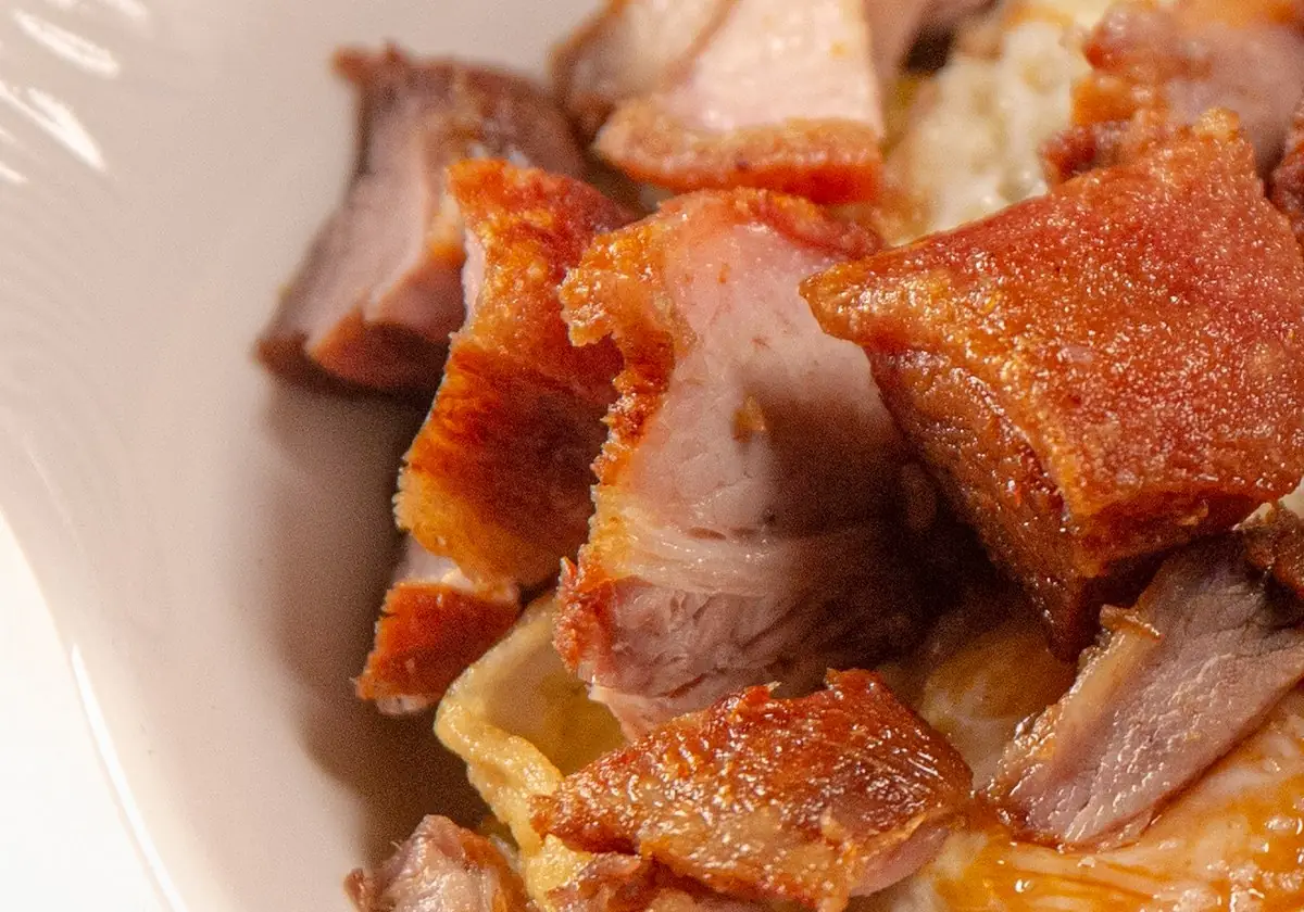 Close-up of crispy fried torreznos (pork belly) chunks over fried eggs on a white plate
