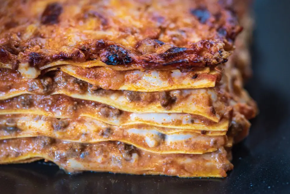 Close-up cross-section of a layered baked lasagna showing pasta sheets, minced meat, and browned cheese top, L'Osteria del Contadino