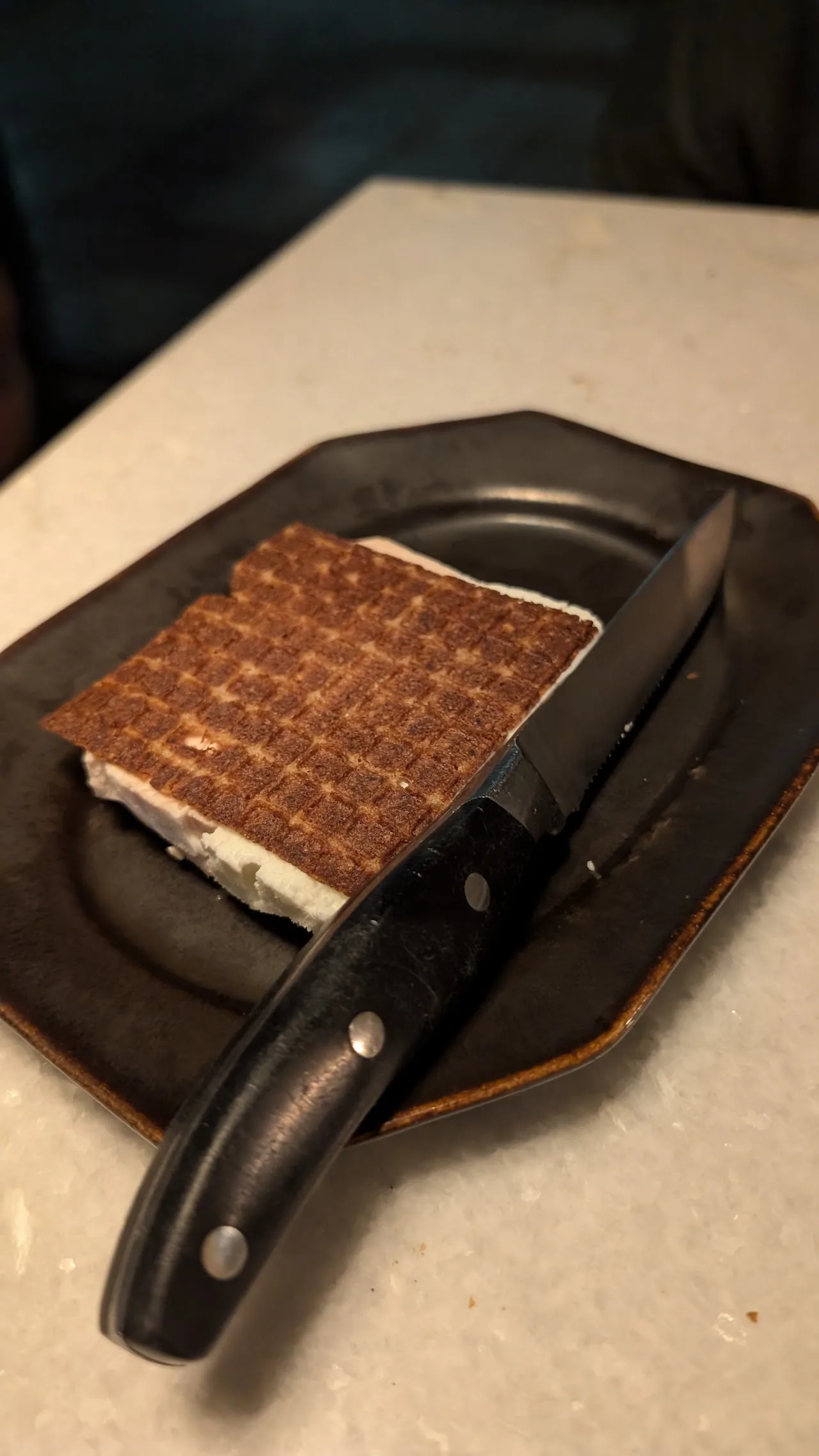 A caramelized dessert on a dark plate with a knife