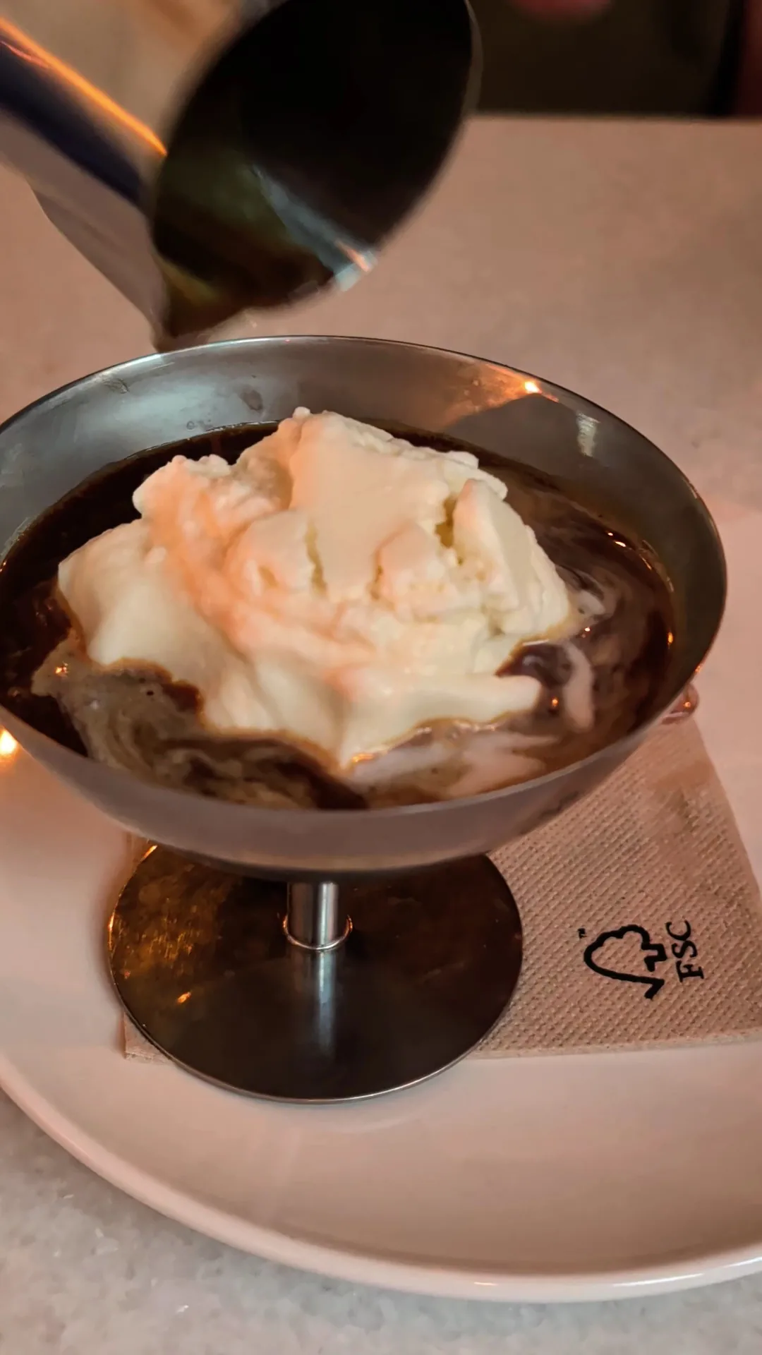 A spoon pouring cream over a chocolate dessert in a glass