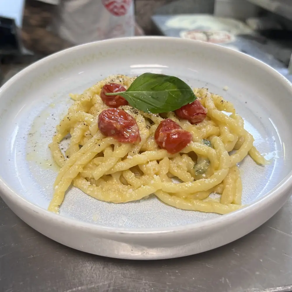 Twist of trofie-style pasta in a creamy cheese sauce topped with roasted cherry tomatoes and a basil leaf on a white plate