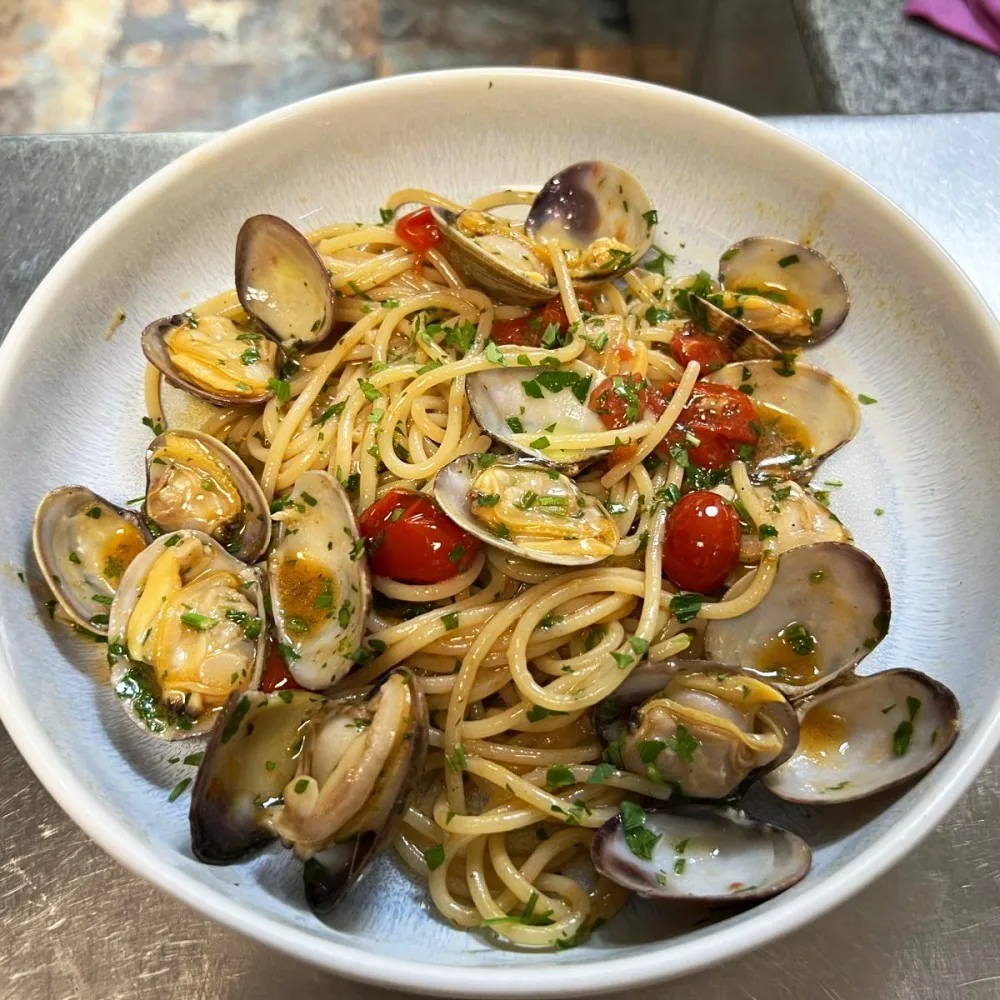 A white bowl of spaghetti with clams and cherry tomatoes