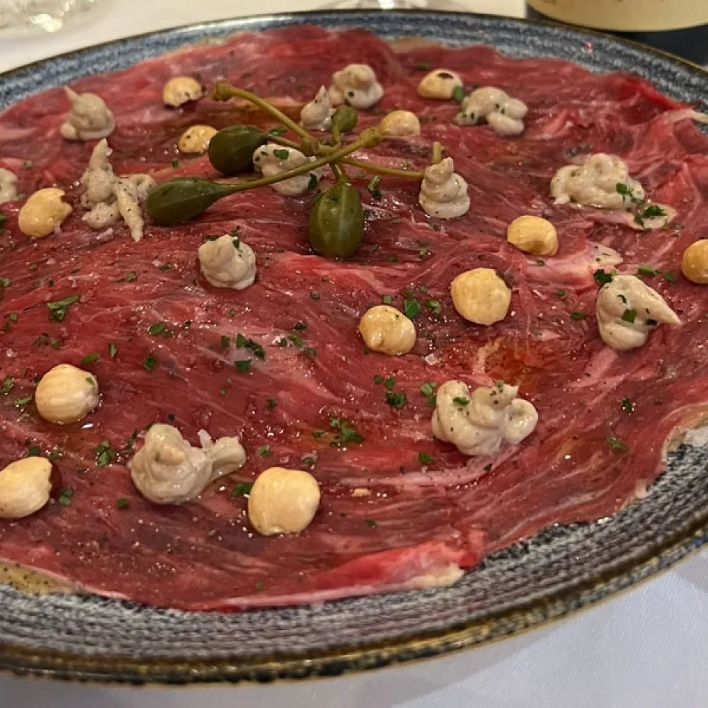 A round plate of thin red carpaccio topped with capers and small mushrooms