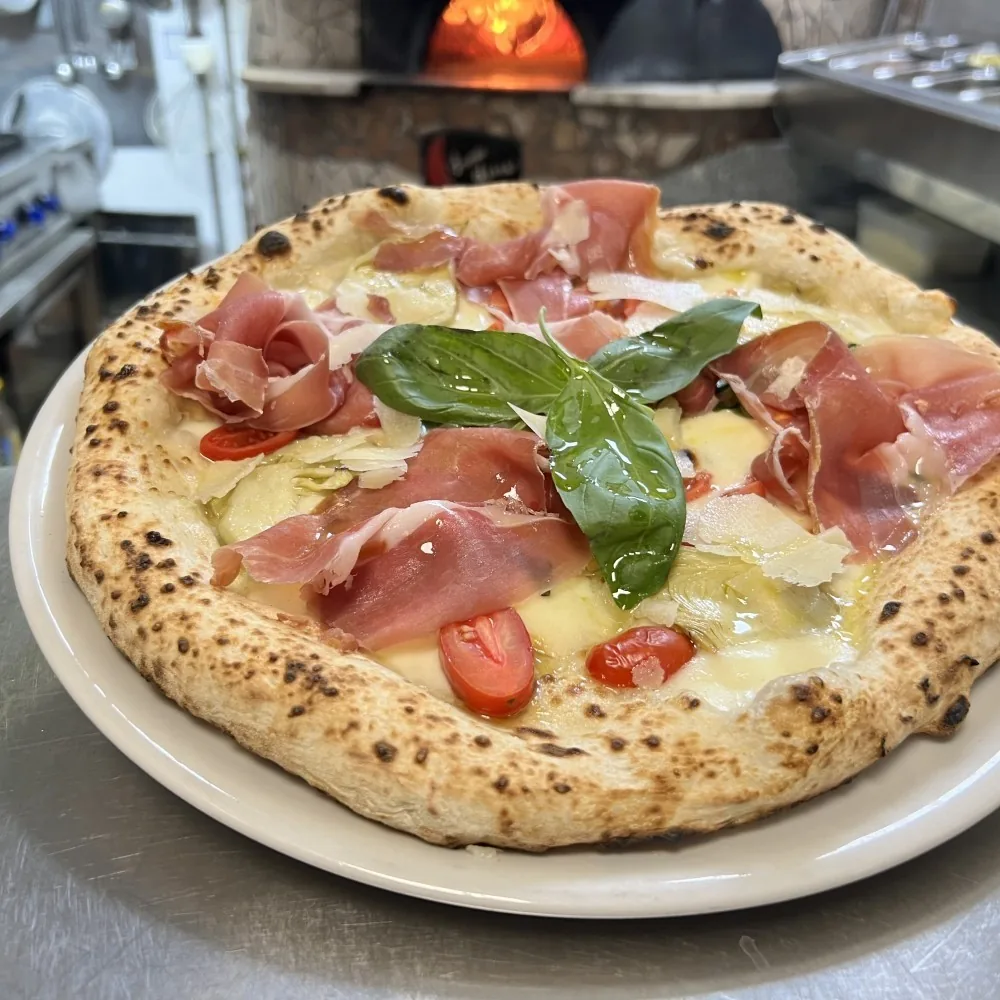 A pizza topped with slices of cured ham and basil leaves on a white plate
