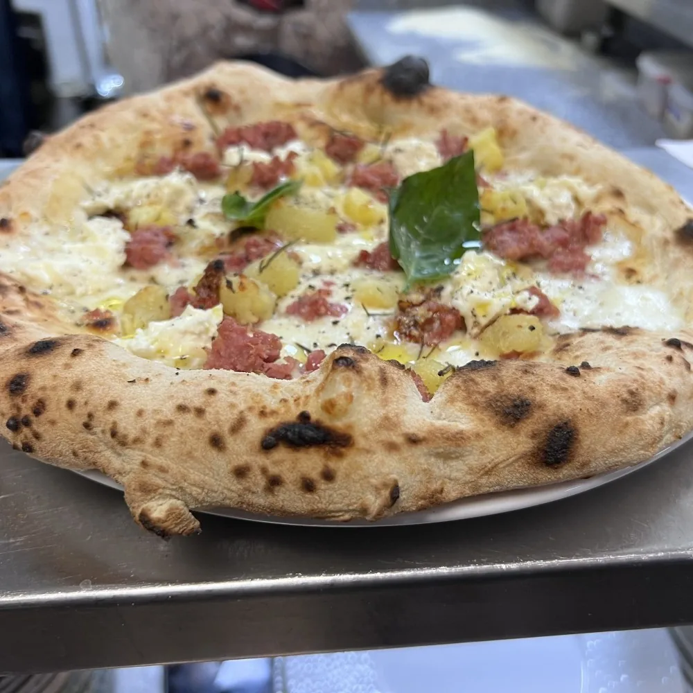 A pizza with white cheese, meat slices and a basil leaf on a plate