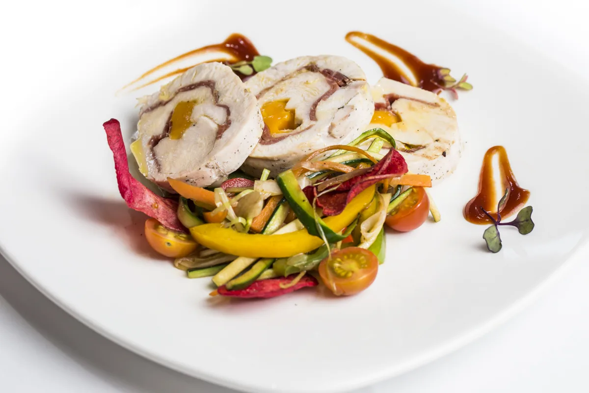 A rolled chicken dish with vegetables and a sauce drizzle