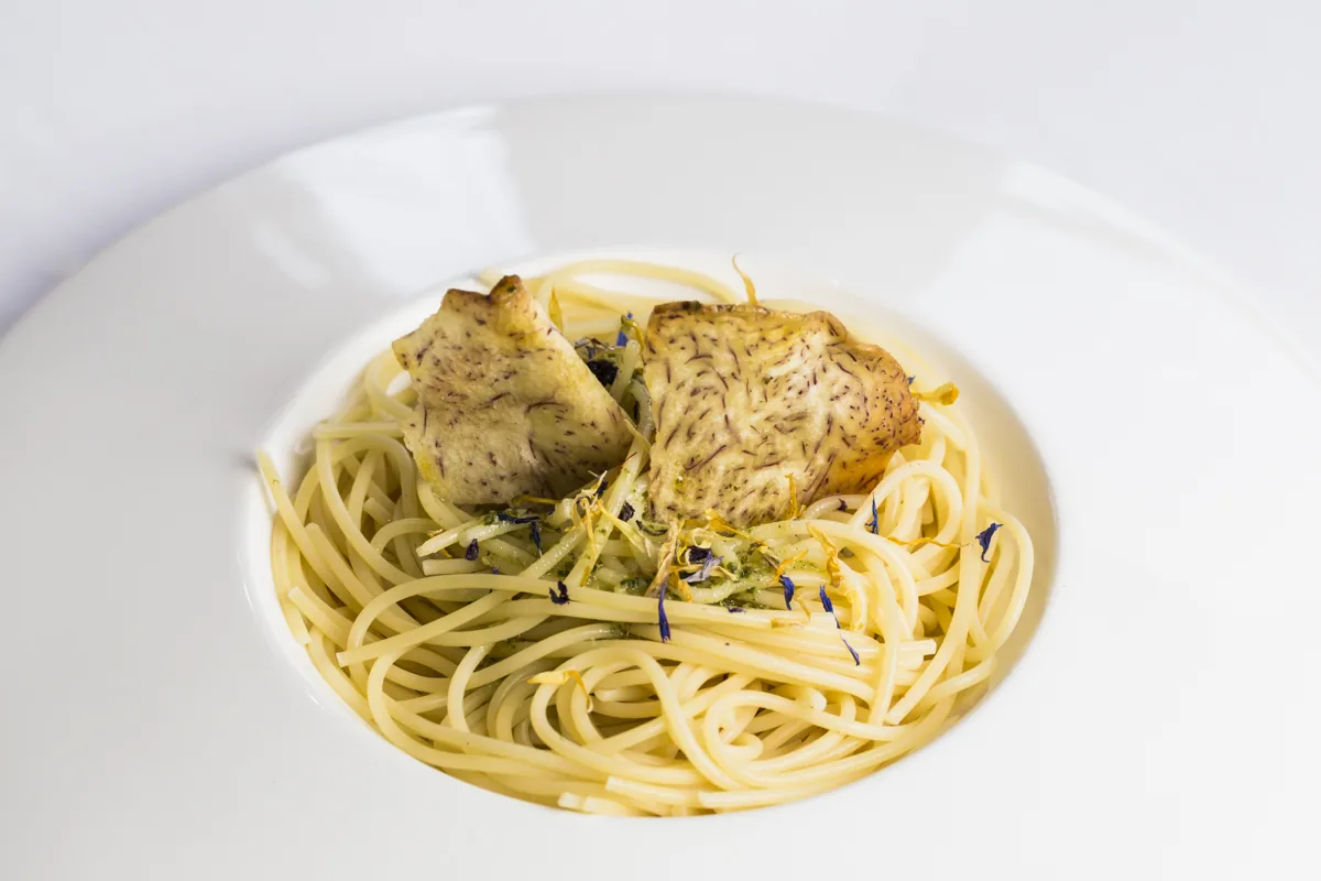 A piece of chicken served over spaghetti