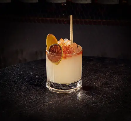 Tumbler cocktail with crushed ice and a dried lime wheel garnish on a dark stone bar top