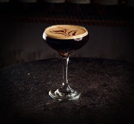 Espresso martini in a coupe glass with a frothy crema top on a dark stone surface