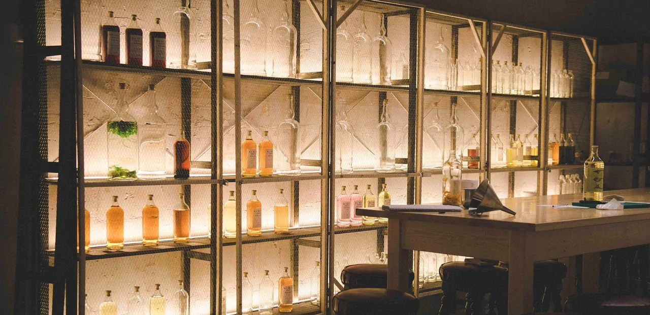 A lit wall of shelves with bottles behind a bar counter
