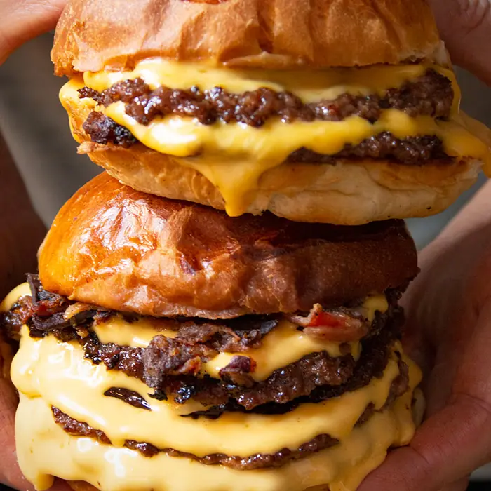 Double smash cheeseburger with melted cheddar and pretzel-style bun held up close, Machaka Burger