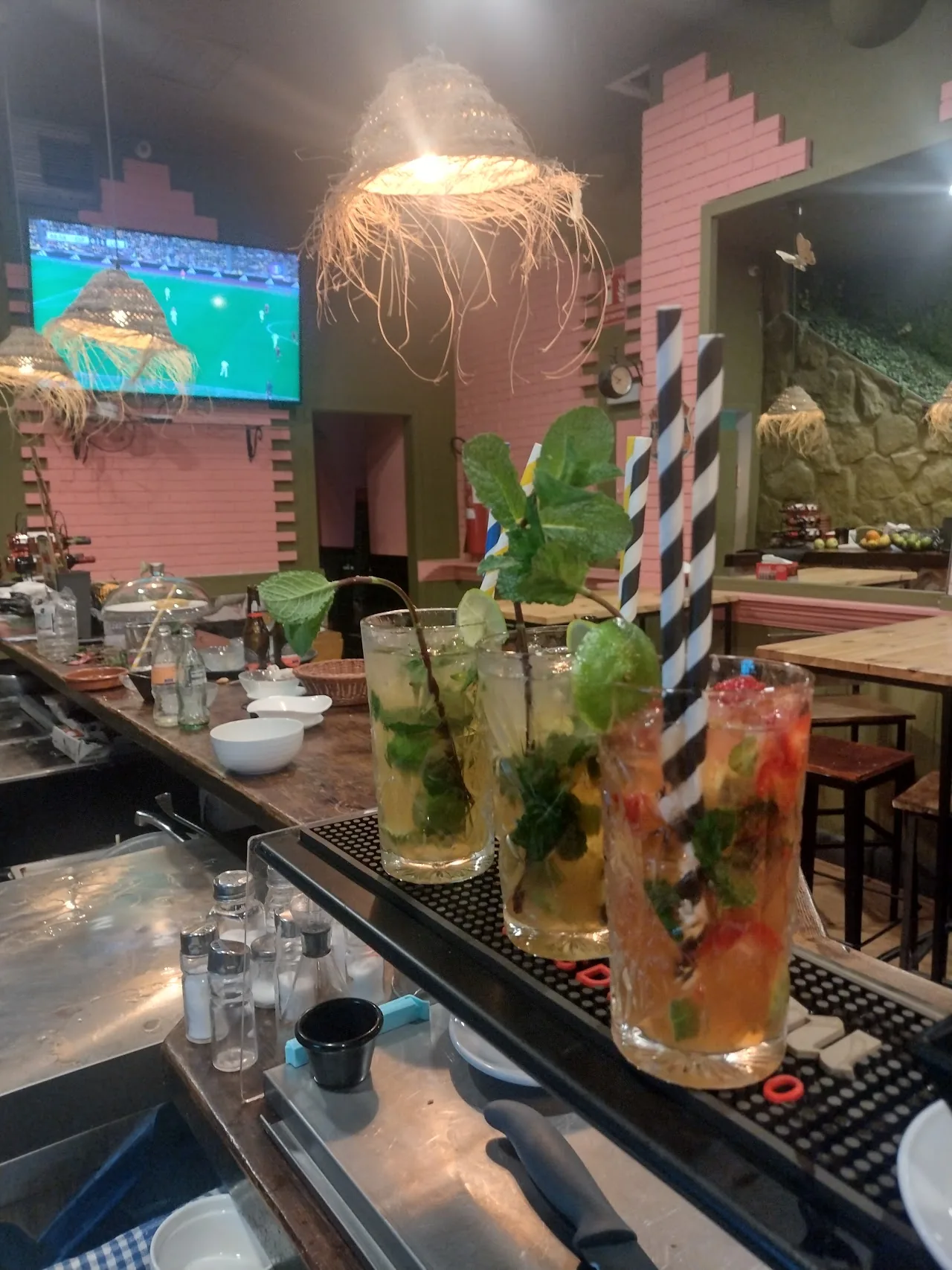 Three mojito-style cocktails with mint and straws lined up on a bar