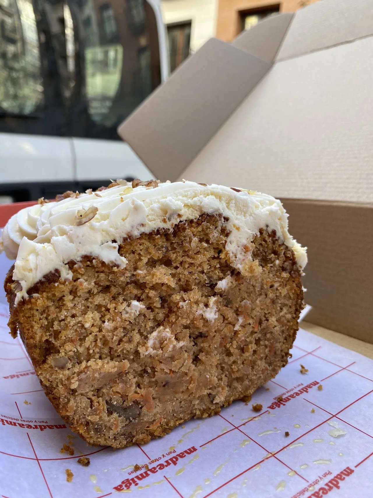 A slice of frosted carrot cake in a takeaway box