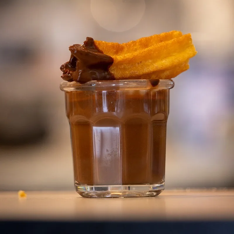 A churro with a chocolate-dipped end resting on a glass of chocolate