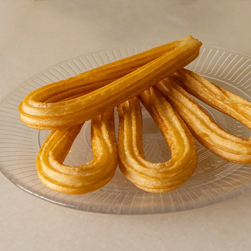Four golden churros on a glass plate