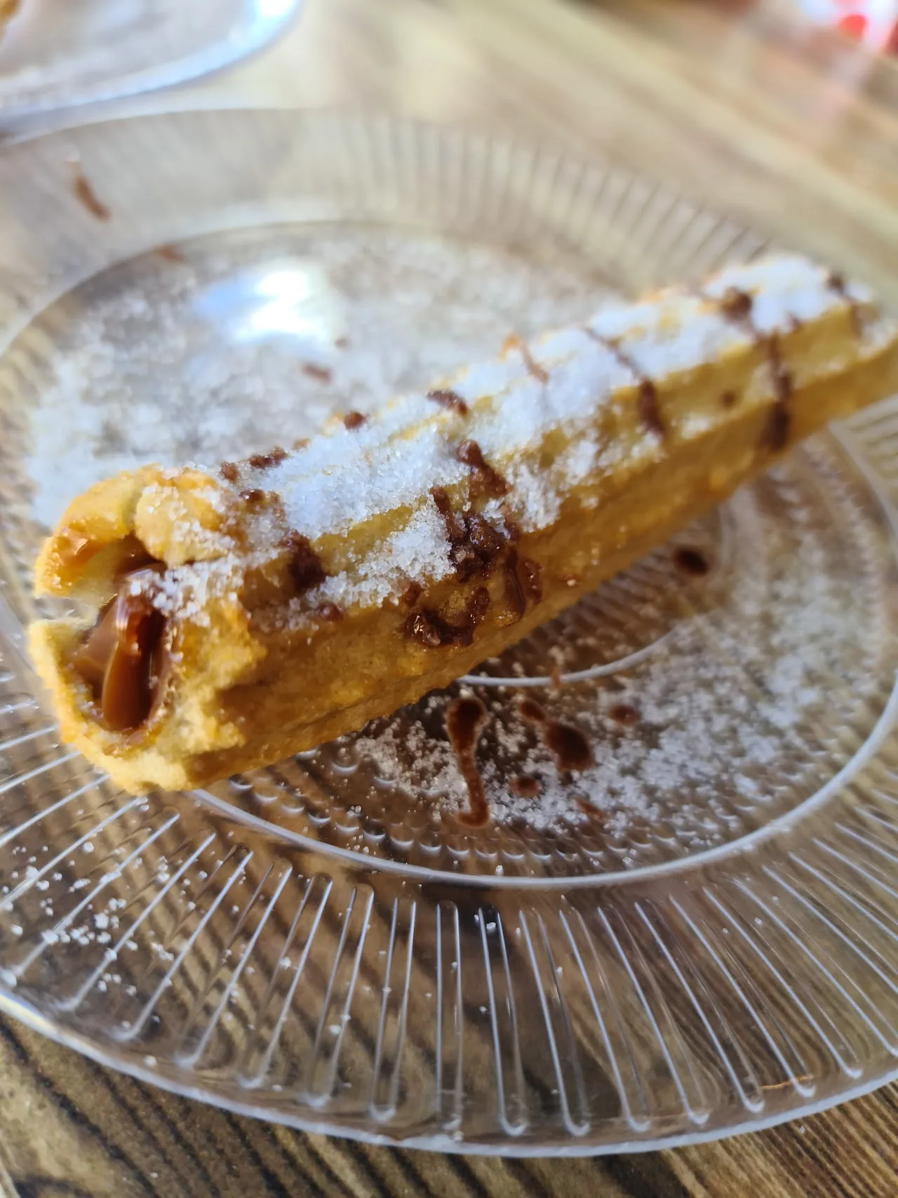 A powdered-sugar churro drizzled with chocolate sauce on a wire rack