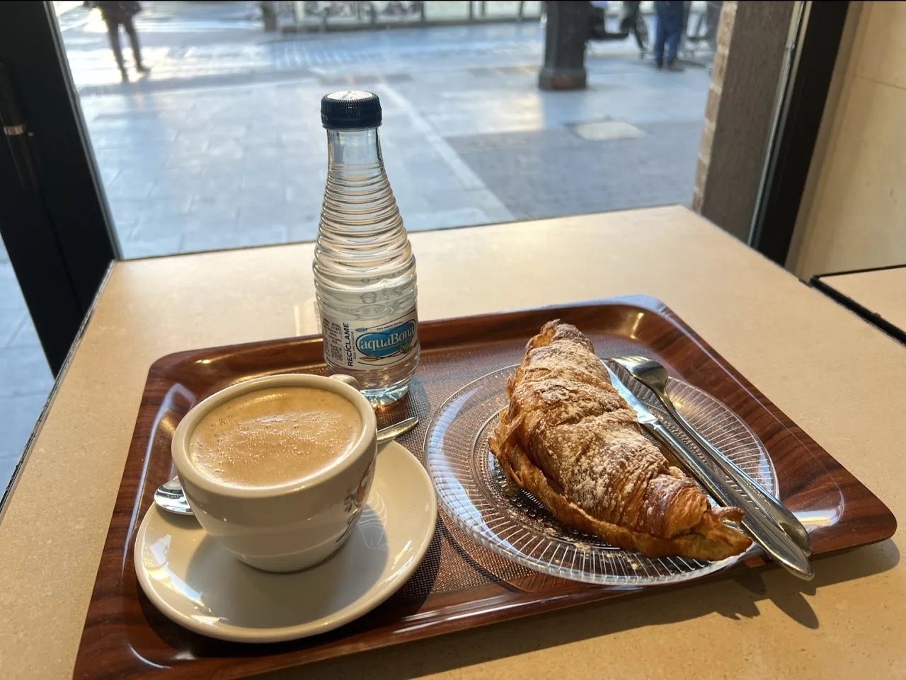 A cup of coffee with a croissant on a breakfast tray
