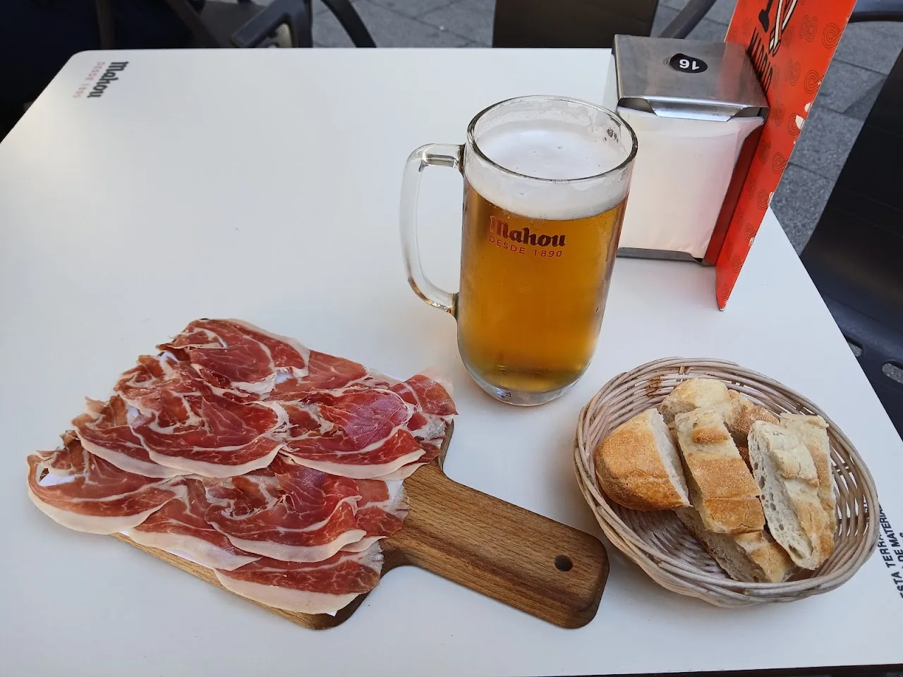 Sliced cured ham with bread and a glass of beer on a board
