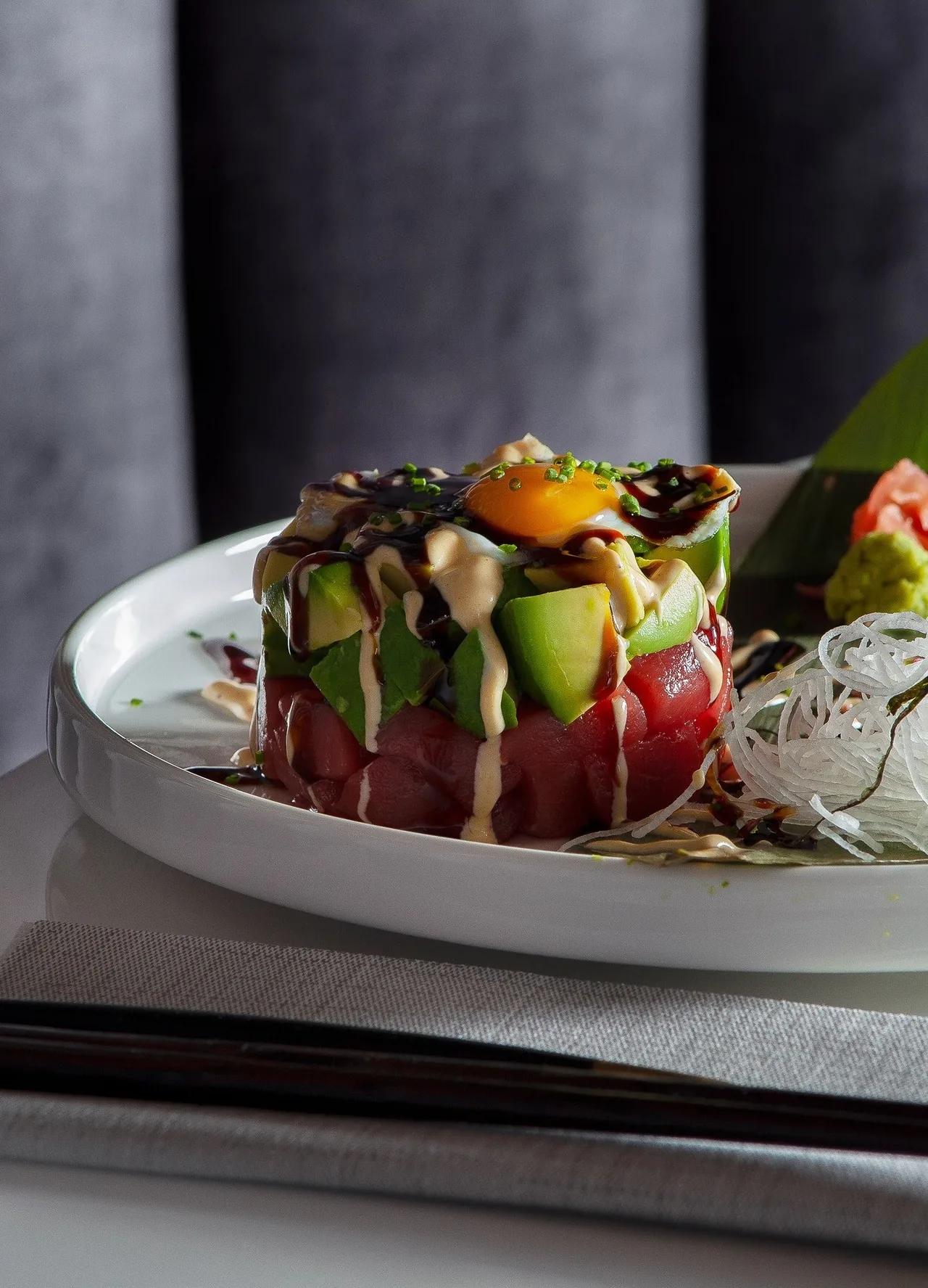 A stacked round dish of tuna and avocado with a sauce on a white plate