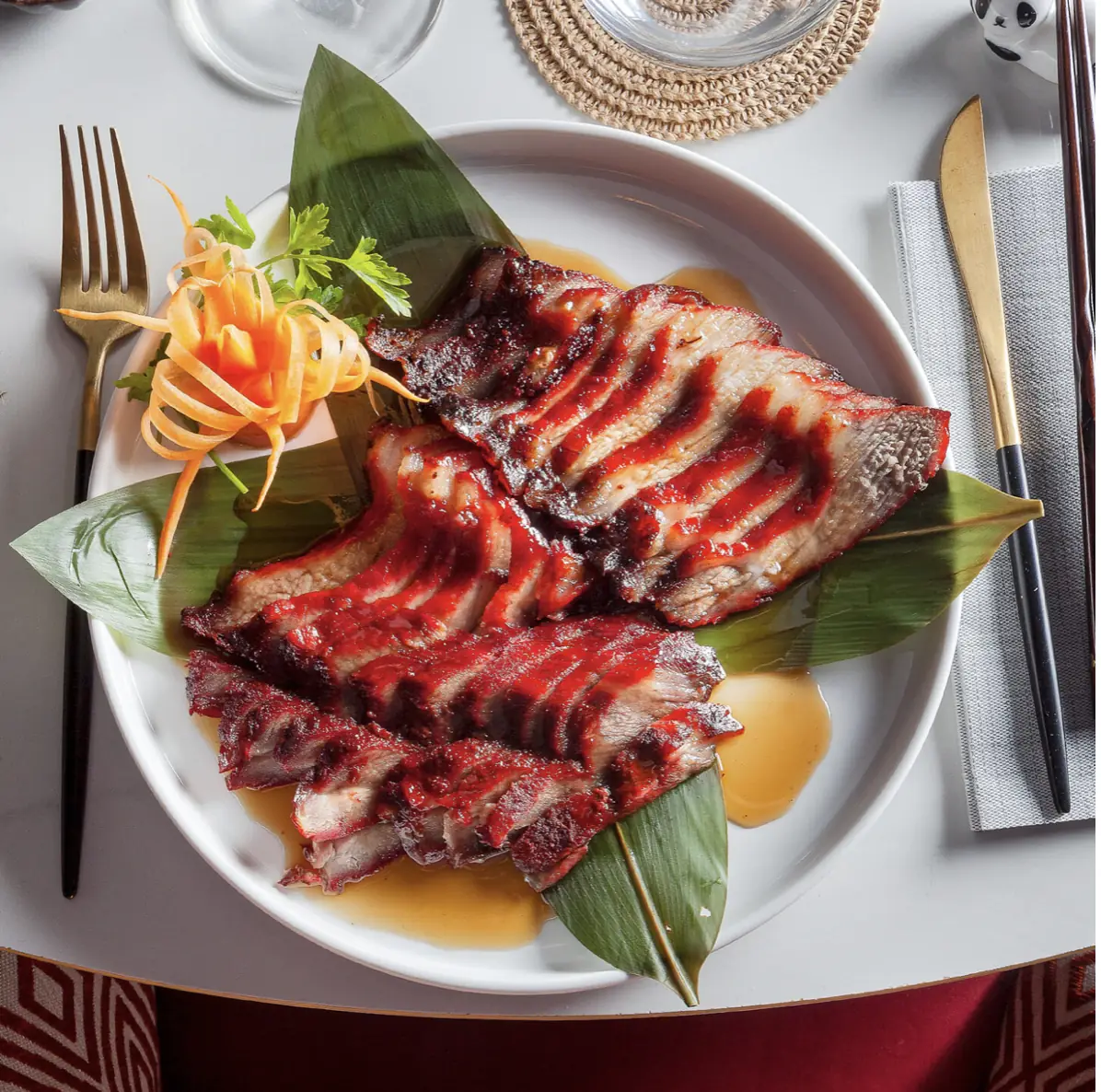 Sliced glazed roasted meat plated on a banana leaf with garnish