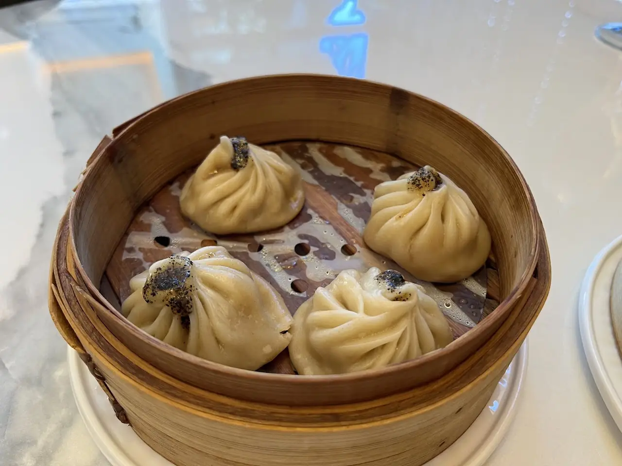 Four soup dumplings with a dark garnish in a bamboo steamer